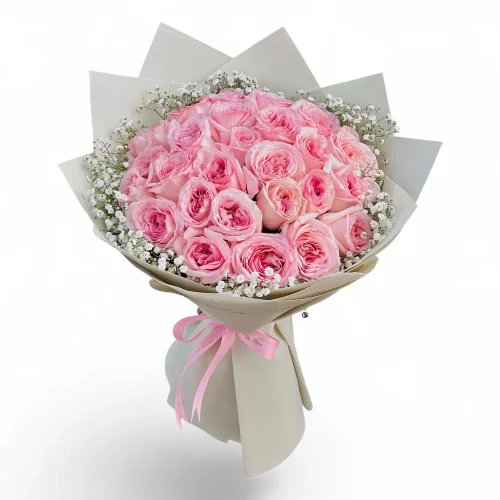 Premium bouquet of soft pink roses arranged in a round shape with white baby’s breath, wrapped in elegant beige paper and tied with a pink ribbon, isolated on a clean white background.