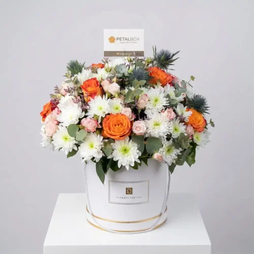 Elegant flower box arrangement with orange roses, white chrysanthemums, blush spray roses, eucalyptus, and fresh greenery in a luxury white floral box.