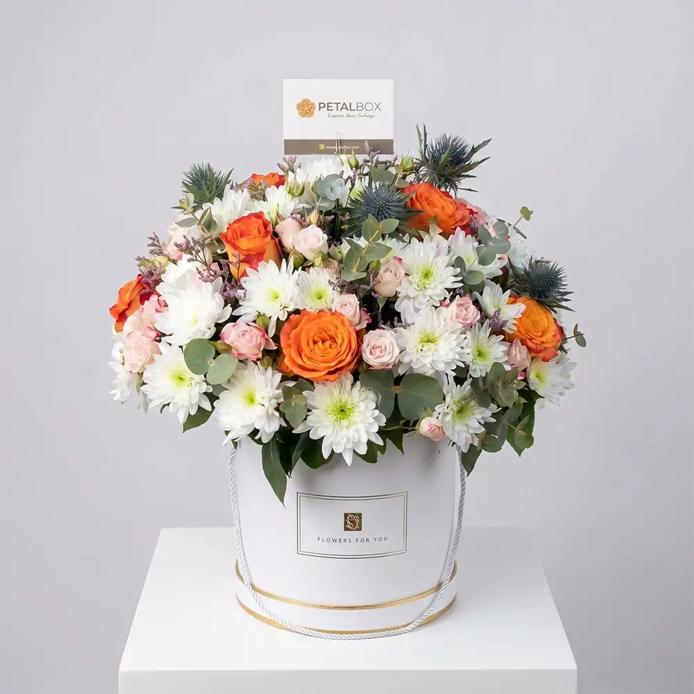 Elegant flower box arrangement with orange roses, white chrysanthemums, blush spray roses, eucalyptus, and fresh greenery in a luxury white floral box.