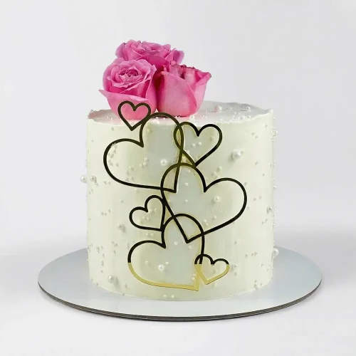 Minimal white cake with cascading gold heart outlines, fresh pink roses on top and pearl dot texture