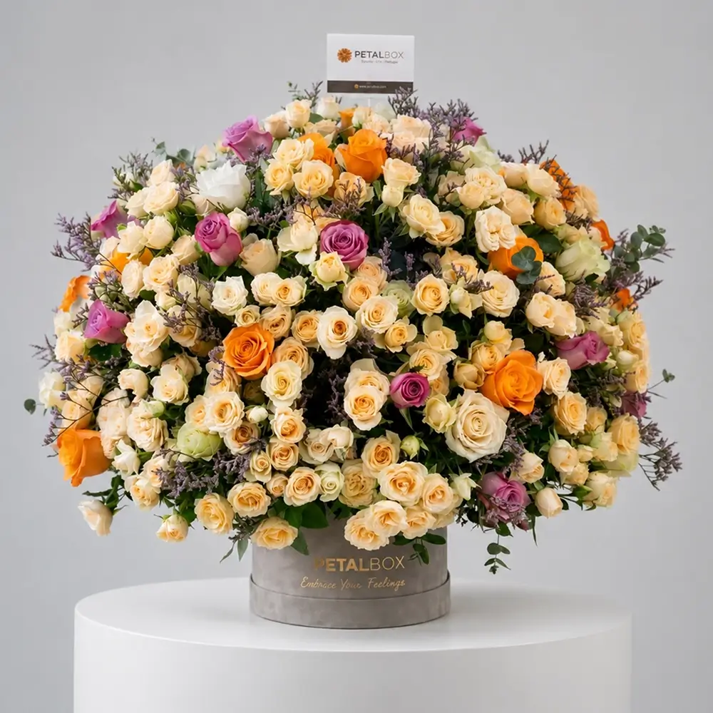 Luxury flower box arrangement with cream spray roses, orange roses, lavender roses, and fresh greenery in an elegant Petal Box floral display.