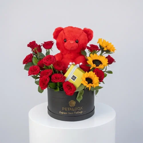 Luxury flower box with red roses, sunflowers, Patchi chocolates, and a red teddy bear in an elegant black Petal Box floral gift arrangement.